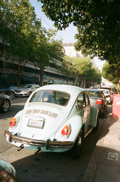 White Volkswagen beetle parked beside the gray car
